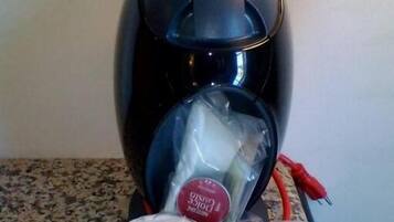 A Dolce Gusto coffee machine with two cups of coffee wrapped in plastic.