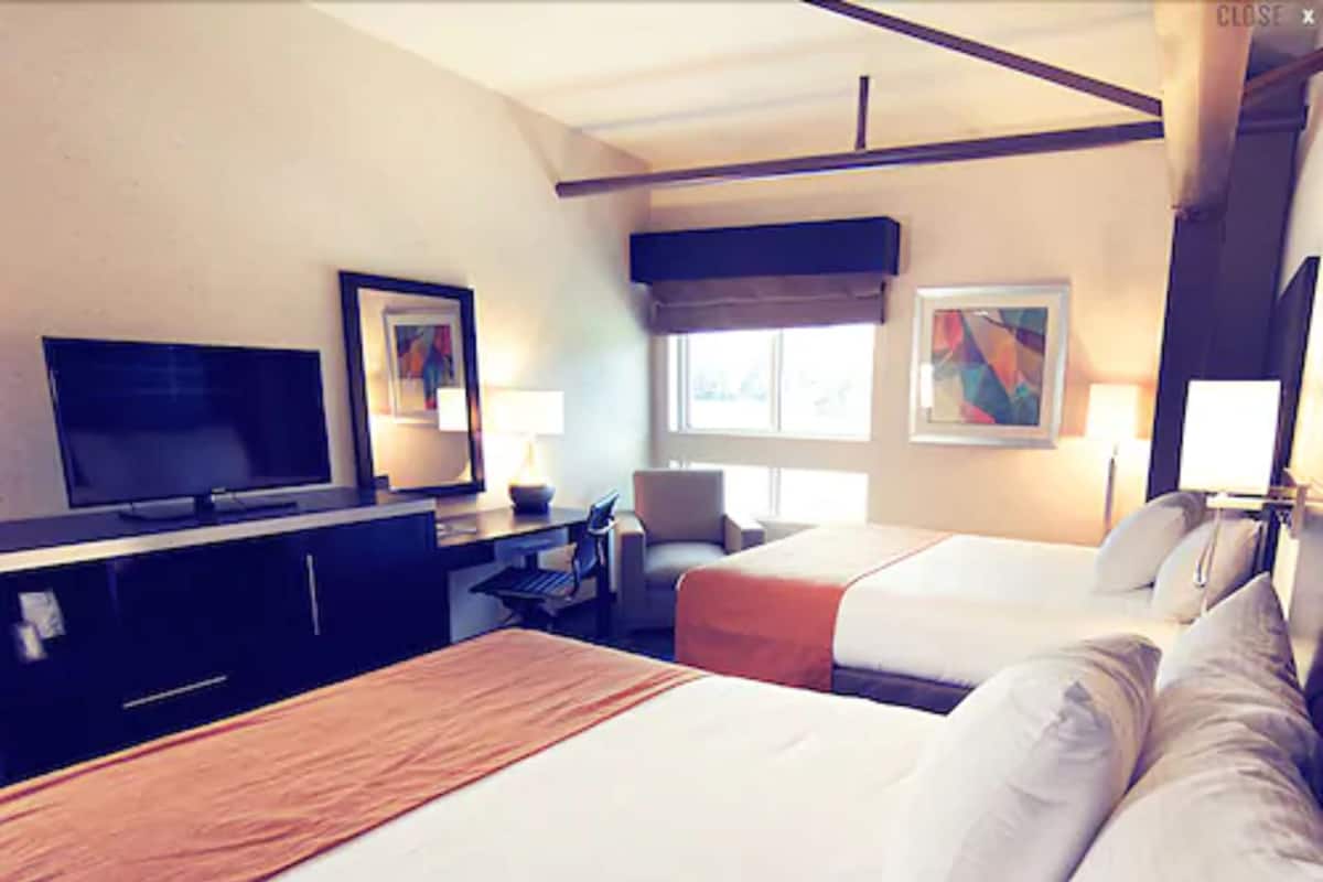 A hotel room with two beds, a TV, a desk, and artwork on the walls.