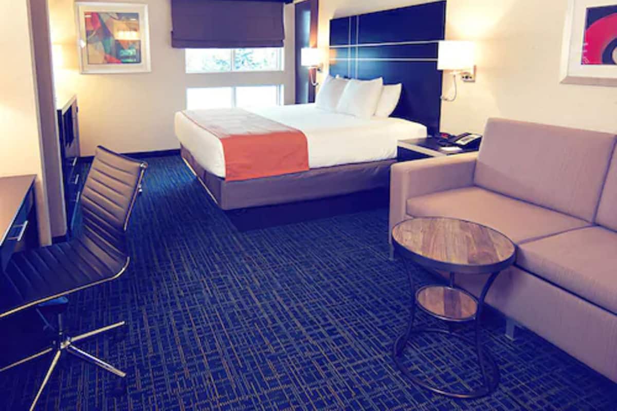 A hotel room with a bed, a desk, a chair, a sofa, and a small table.