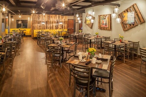 A restaurant with wooden tables and chairs, hanging light fixtures, and a yellow accent wall. - Warehouse Hotel (Manheim)