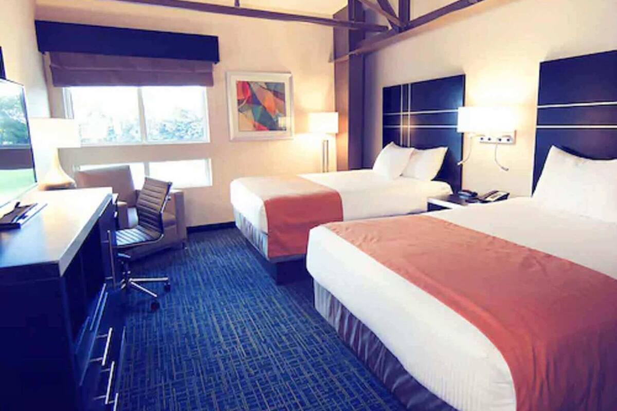 A hotel room with two beds, a desk, a chair, and a window.