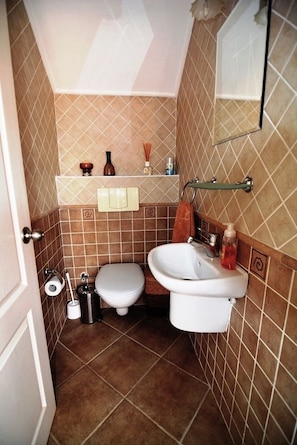 A small bathroom with a toilet, sink, and mirror. There are toiletries on the sink and a towel hanging on the wall.
