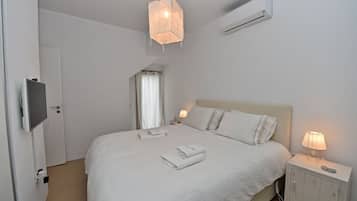 A neatly made bed with white linens, a bedside lamp, and a wall-mounted air conditioner.
