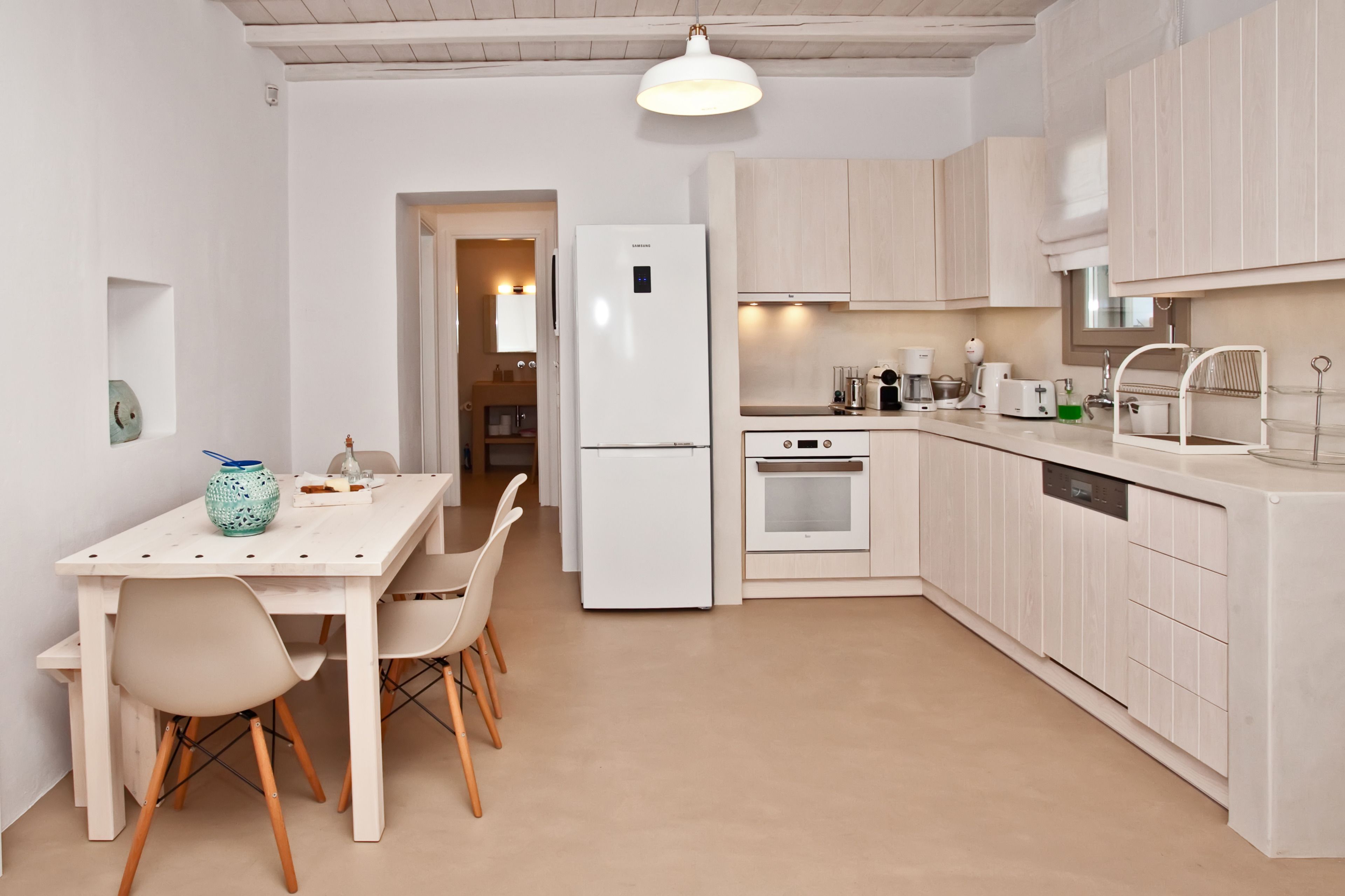 Une cuisine moderne avec des meubles blancs, une table à manger avec des chaises, un réfrigérateur, un four et un lave-vaisselle.