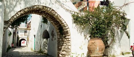 Una estrecha calle con un arco de piedra, edificios blancos y una gran maceta de terracota.