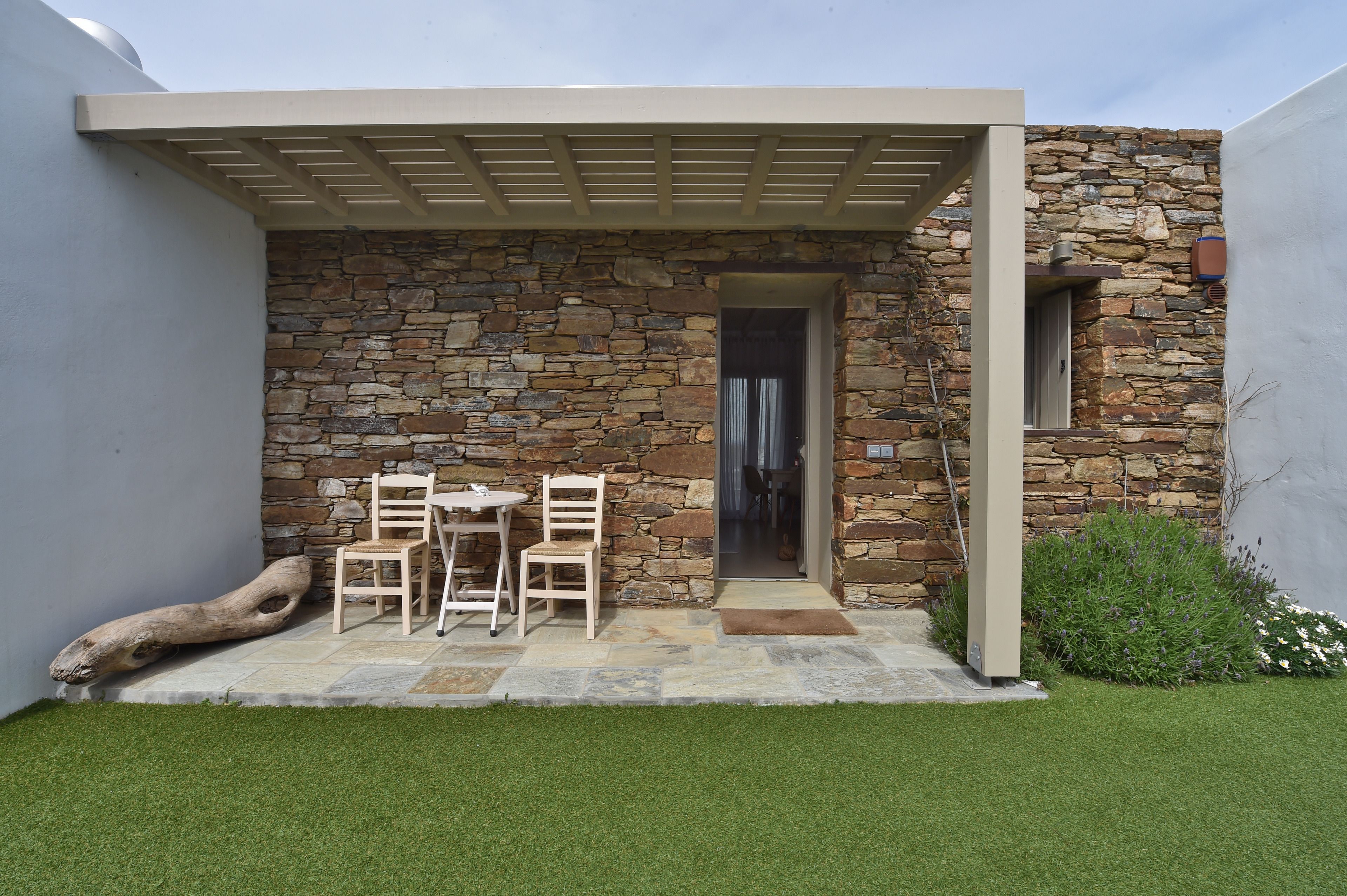 Un edificio moderno con fachada de piedra, un patio cubierto con una mesa y sillas, y una ventana pequeña.