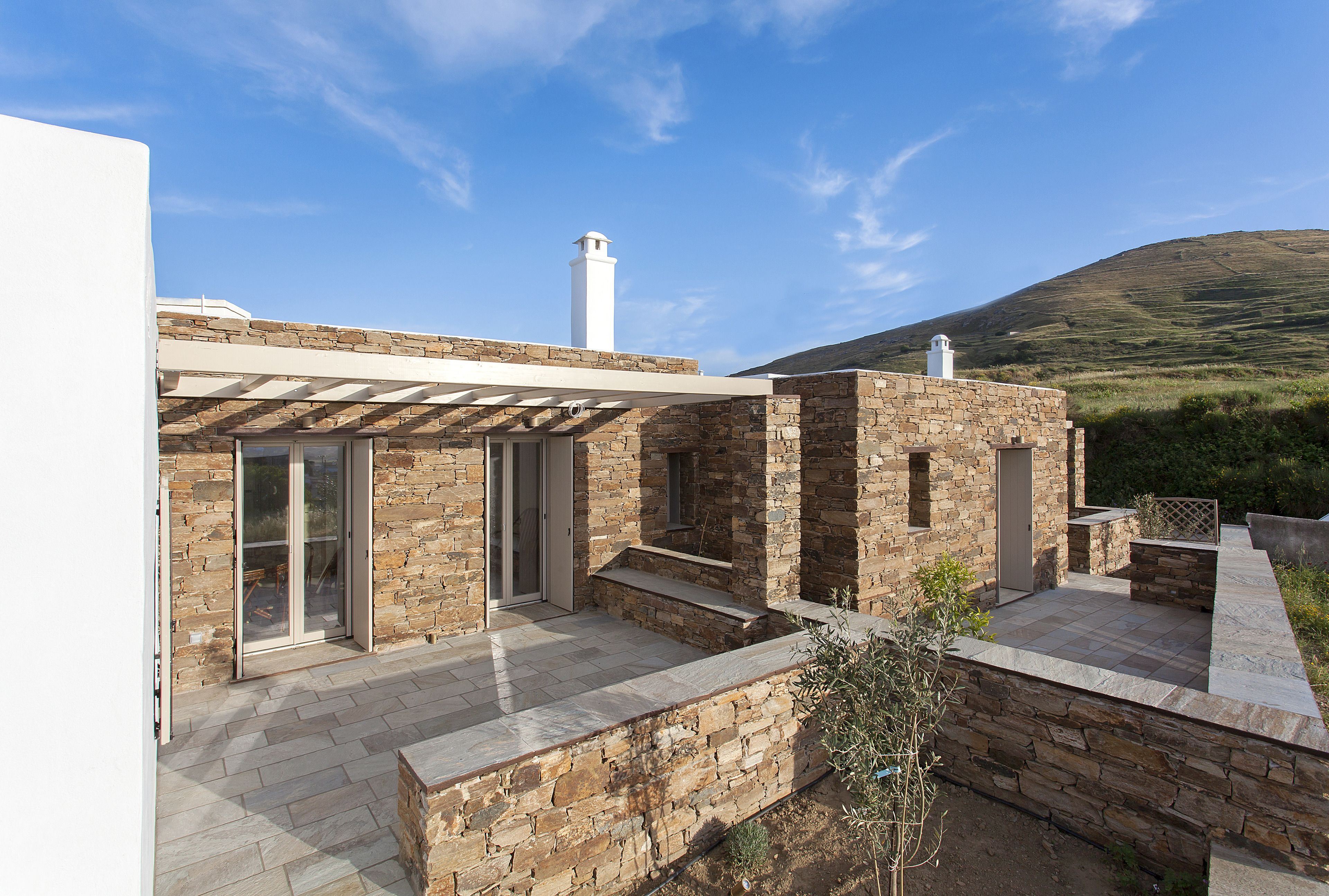 A modern house with stone walls, a covered patio, and a view of the countryside.