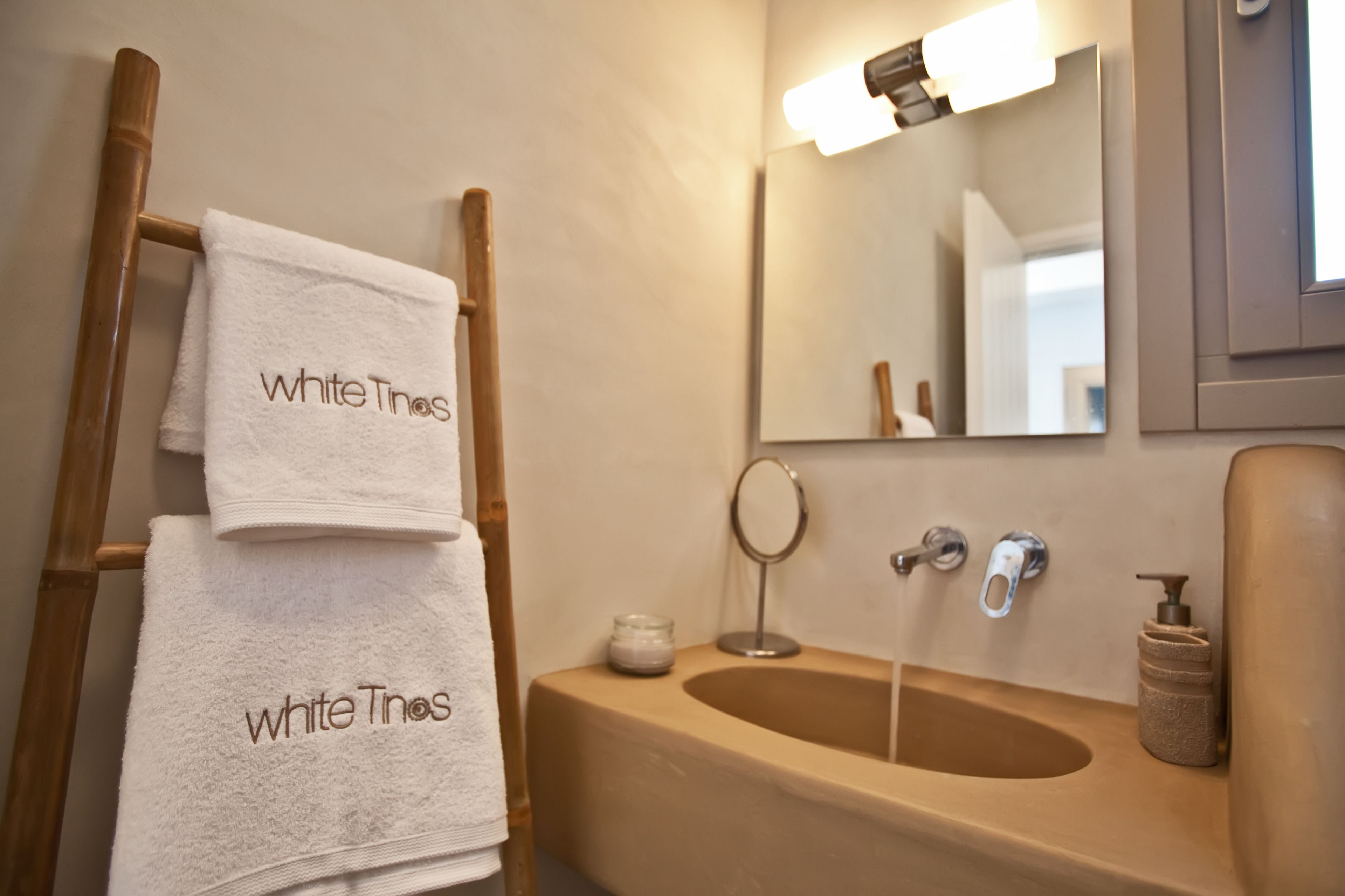 Une salle de bain avec un porte-serviettes en bois sur lequel sont posées deux serviettes, un lavabo avec un miroir et un distributeur de savon.