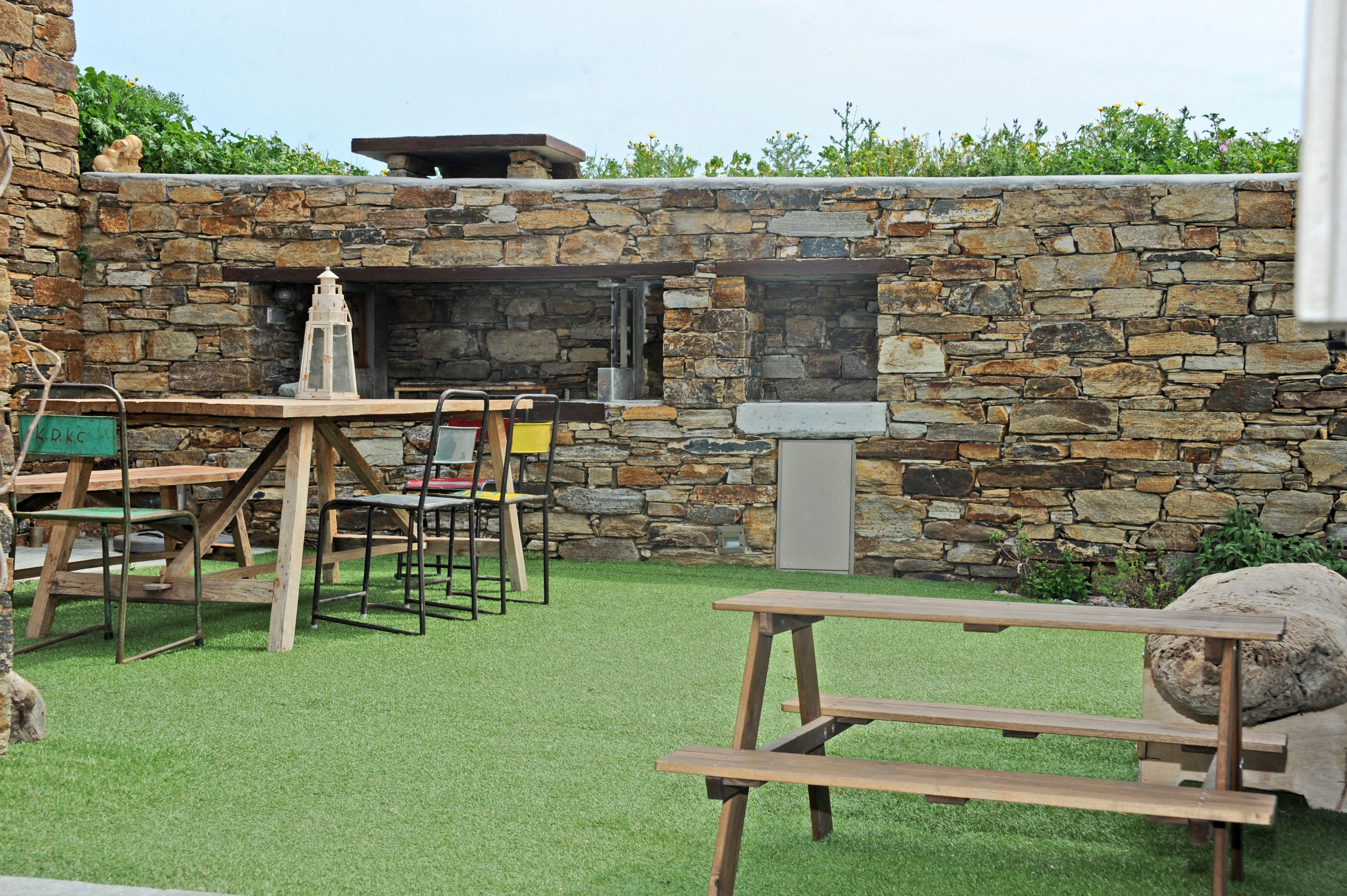 An outdoor patio with stone walls, a wooden table, chairs, and a grill.