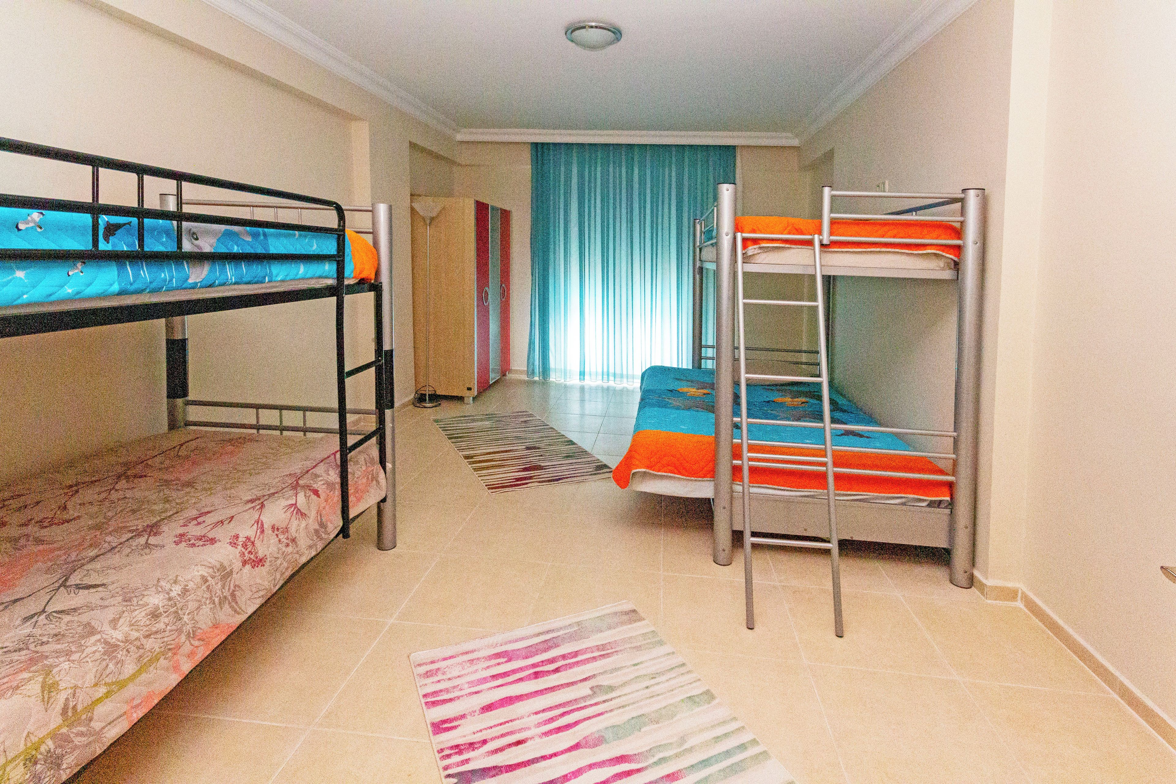 A dormitory room with bunk beds, a striped rug, and a blue curtain.