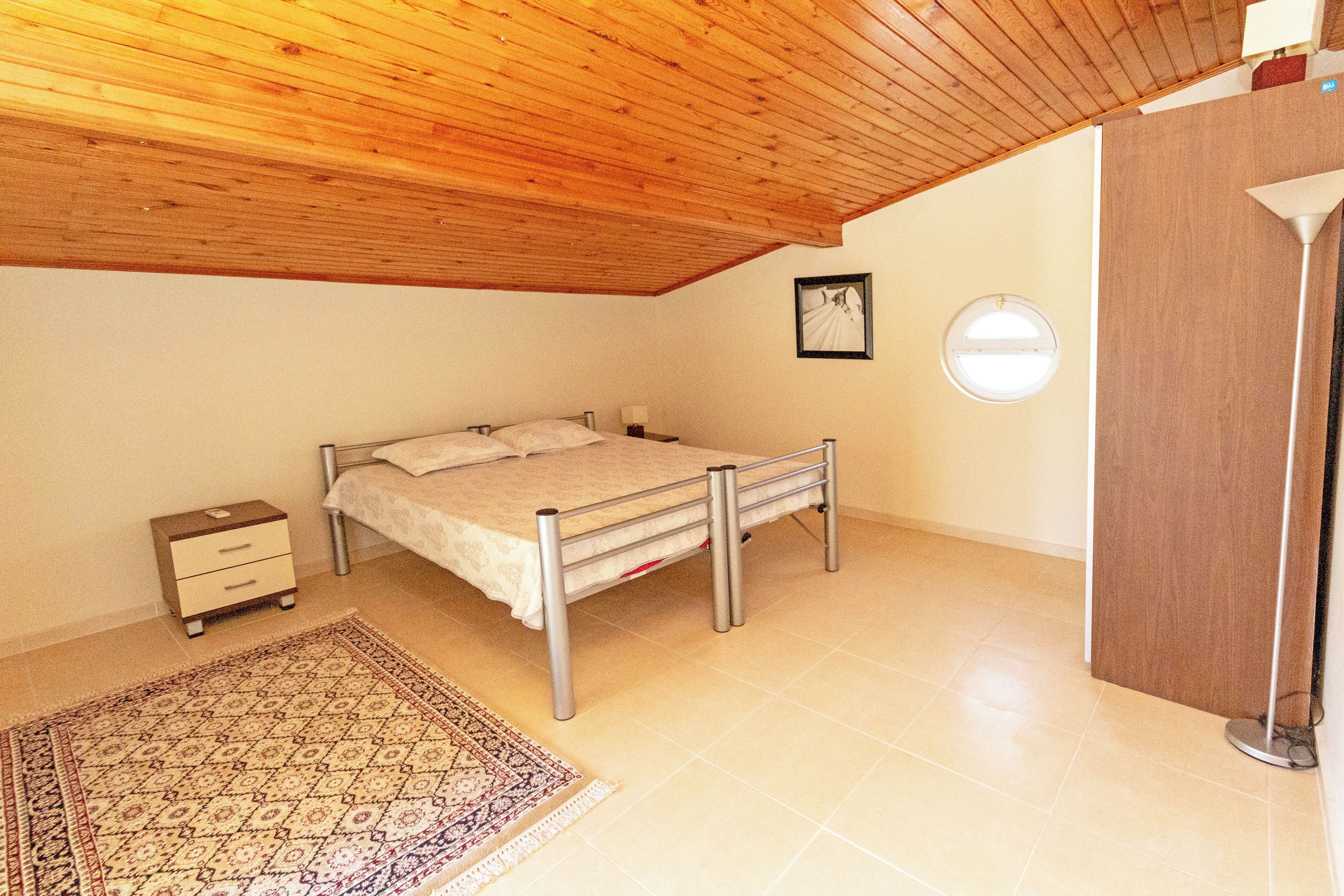 Quarto com cama, mesa de cabeceira, luminária e teto de madeira.