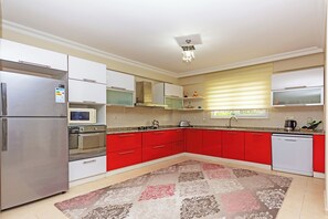 A modern kitchen with red cabinets, stainless steel appliances, and a patterned rug. - Paradise Town Villa Alison (Serik)