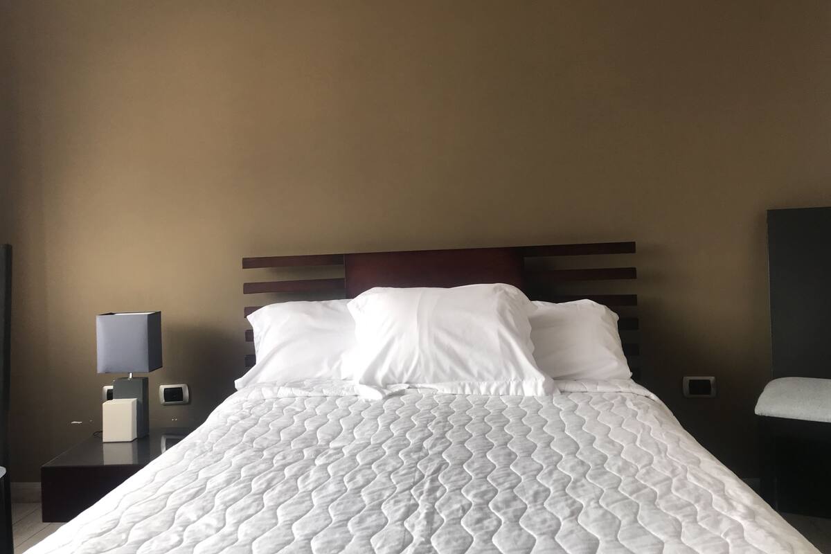 A neatly made bed with a white quilt, a wooden headboard, and a bedside table with a lamp.