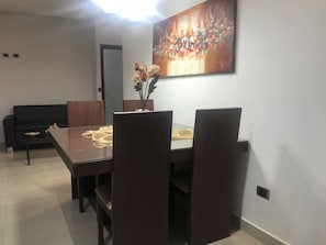 Un comedor con una mesa y sillas de madera oscura, un florero con flores secas y un cuadro abstracto grande en la pared.