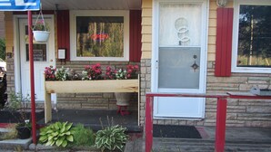 A house with a front porch, a door with a number plate, and a bench with flowers. - The New Elgin Motel (Saint Thomas)