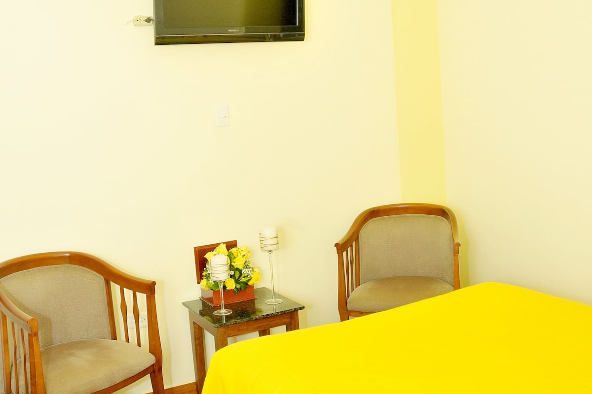 A hotel room with two beds, a television, a small table with a vase of flowers, and a chandelier.