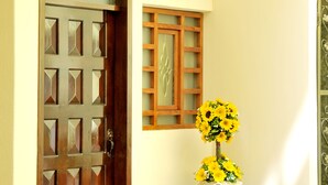 A wooden door with a geometric pattern, a small table with a vase of yellow flowers, and a decorative window with a lattice design. - Hotel Margarita 2 (Quito)