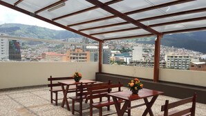 A terrace with wooden furniture and a view of a cityscape. - Hotel Margarita 2 (Quito)