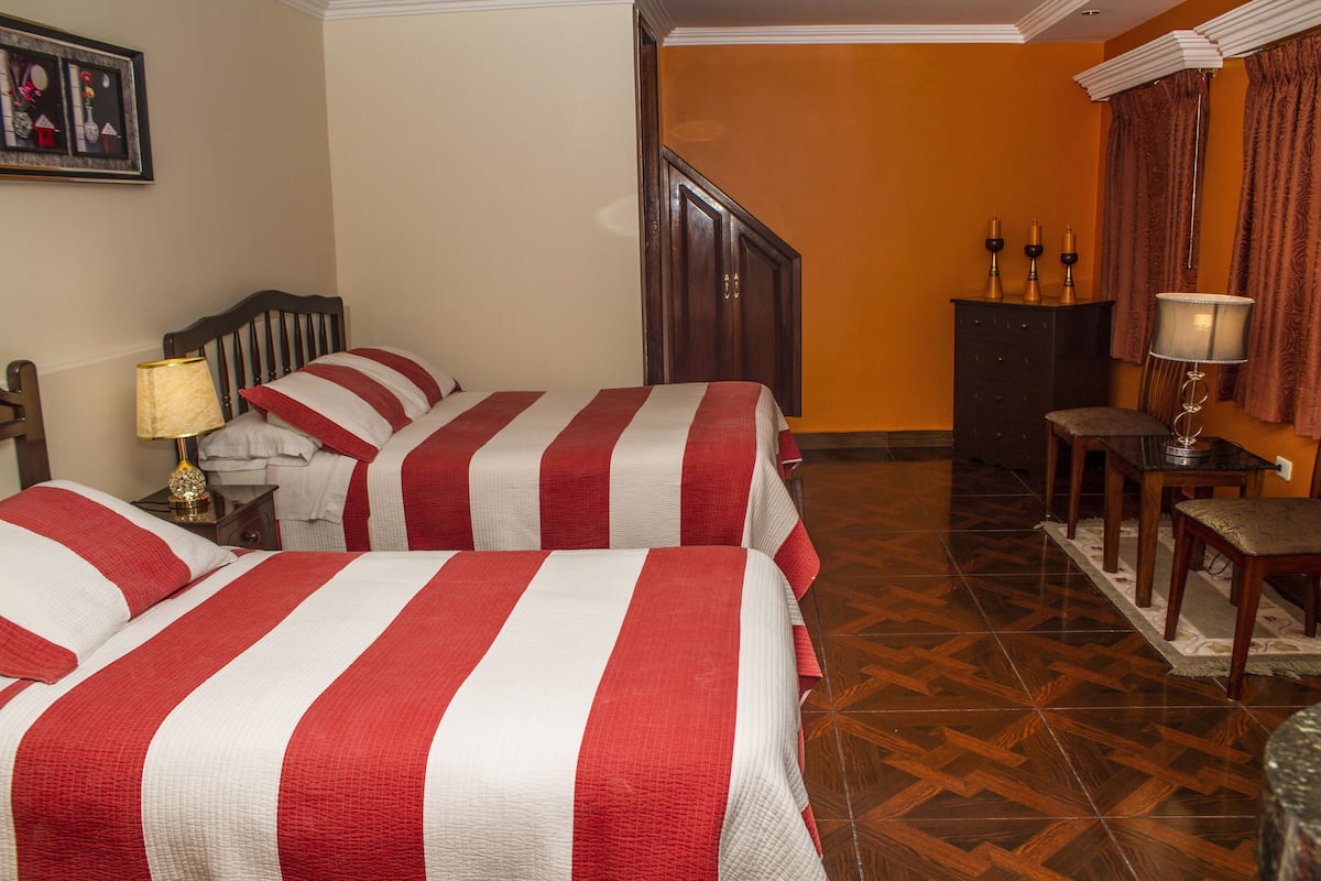 A hotel room with two beds, a wooden floor, a desk, and a chair.