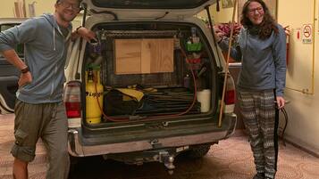 A vehicle with its trunk open, revealing a toolbox, a gas canister, and a wooden board.