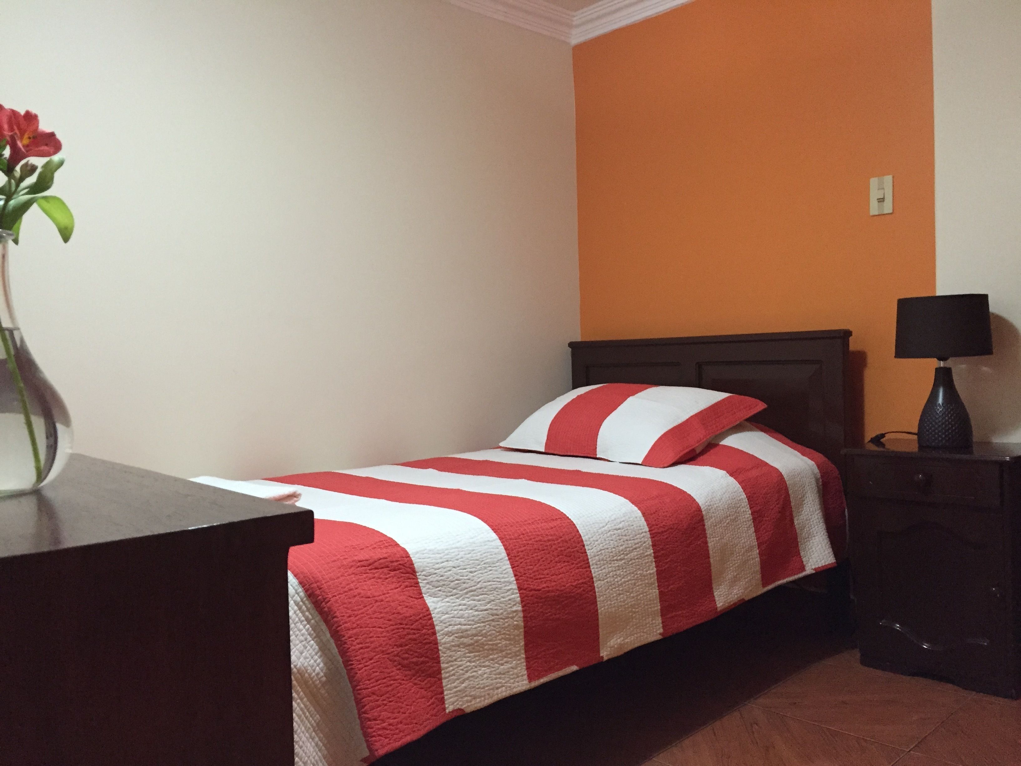 A bedroom with a bed, a nightstand, a lamp, and a vase with a flower.