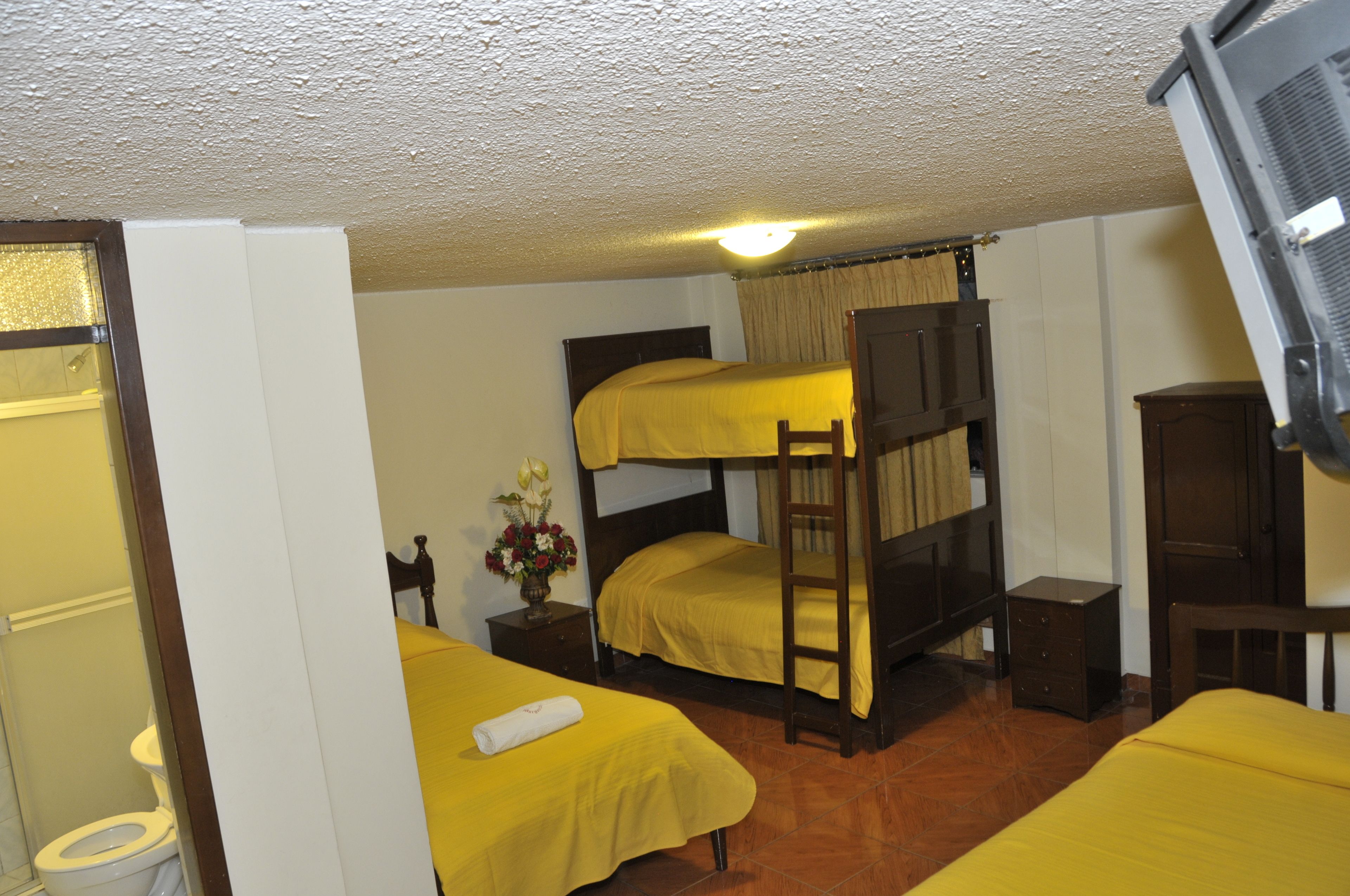 A room with bunk beds, a small bedside table with a vase, and a wooden wardrobe.