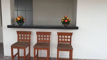 A reception area with a counter, three wooden chairs, and two flower arrangements.