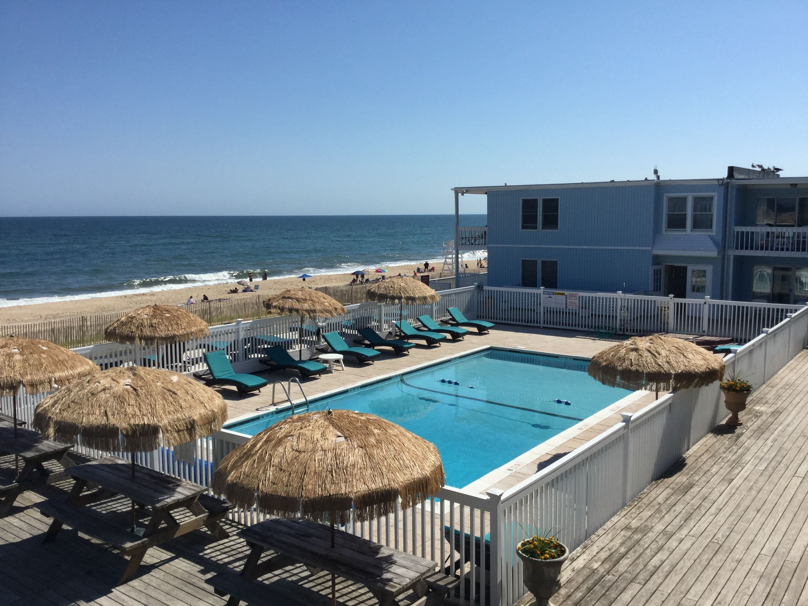 A pool area with lounge chairs and umbrellas, overlooking a beach and ocean.
