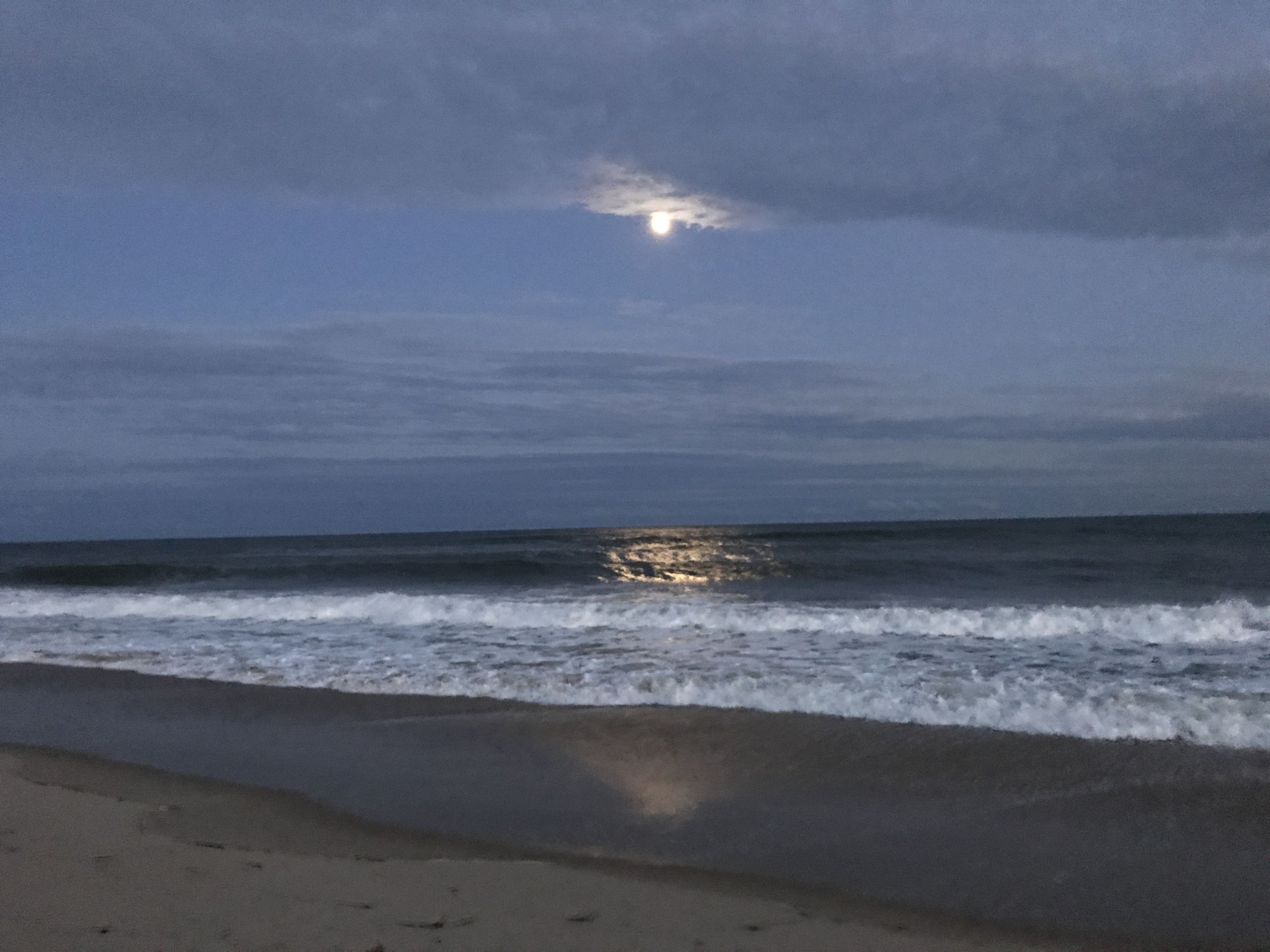 Une plage avec des vagues et une lune dans le ciel.