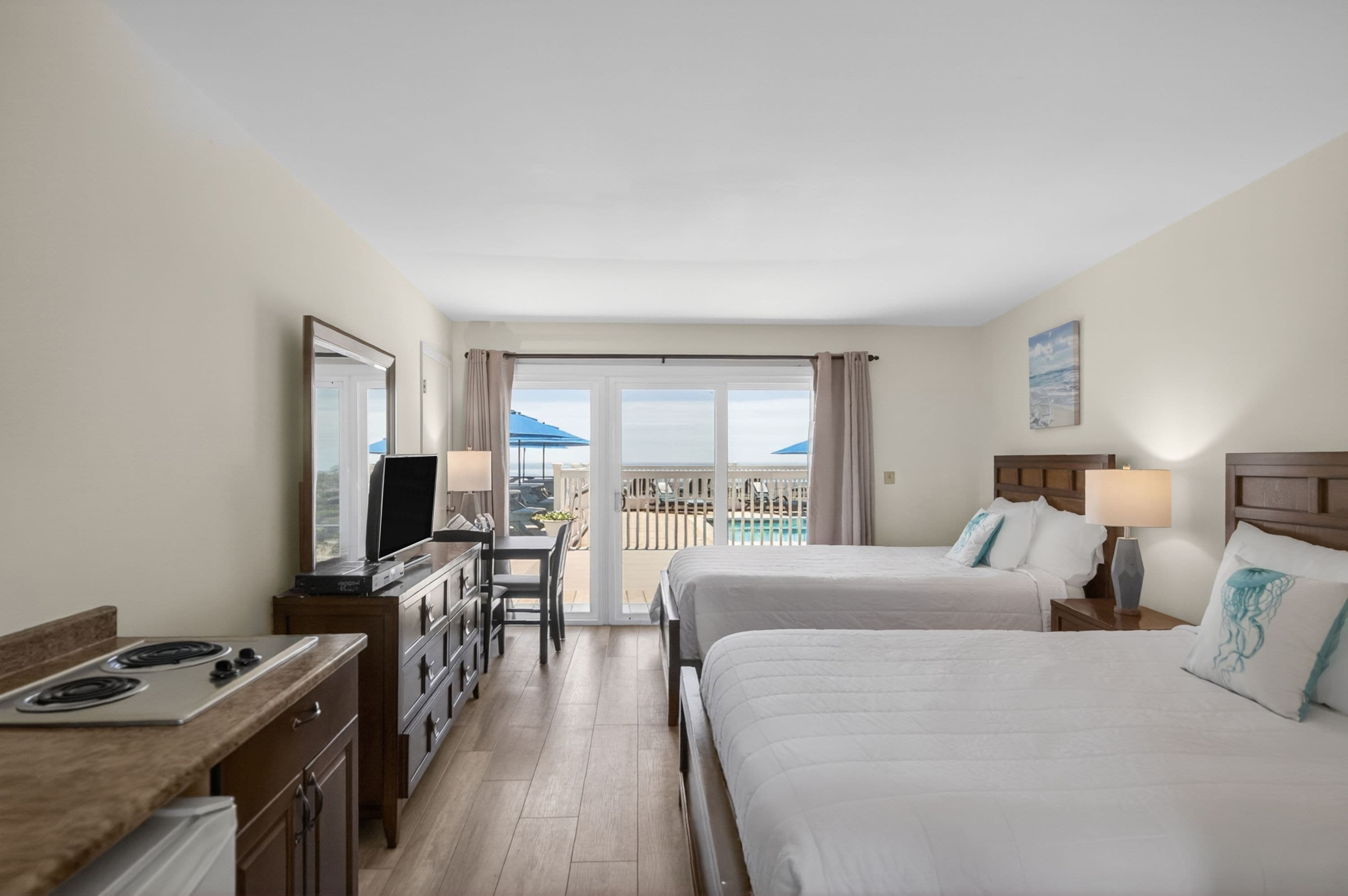 Habitación de hotel con dos camas, un escritorio, un televisor y un balcón con vistas al mar.