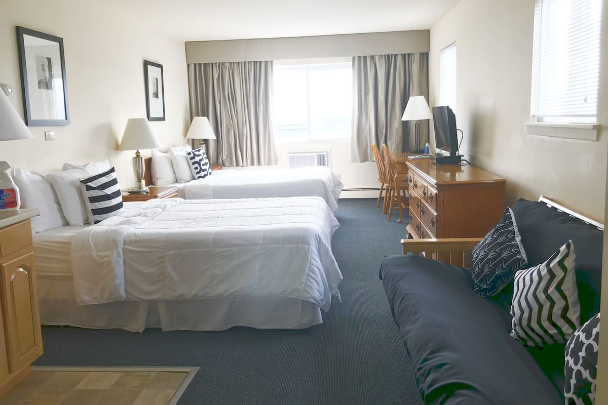 A hotel room with two beds, a sofa, a desk with a lamp, and a television.