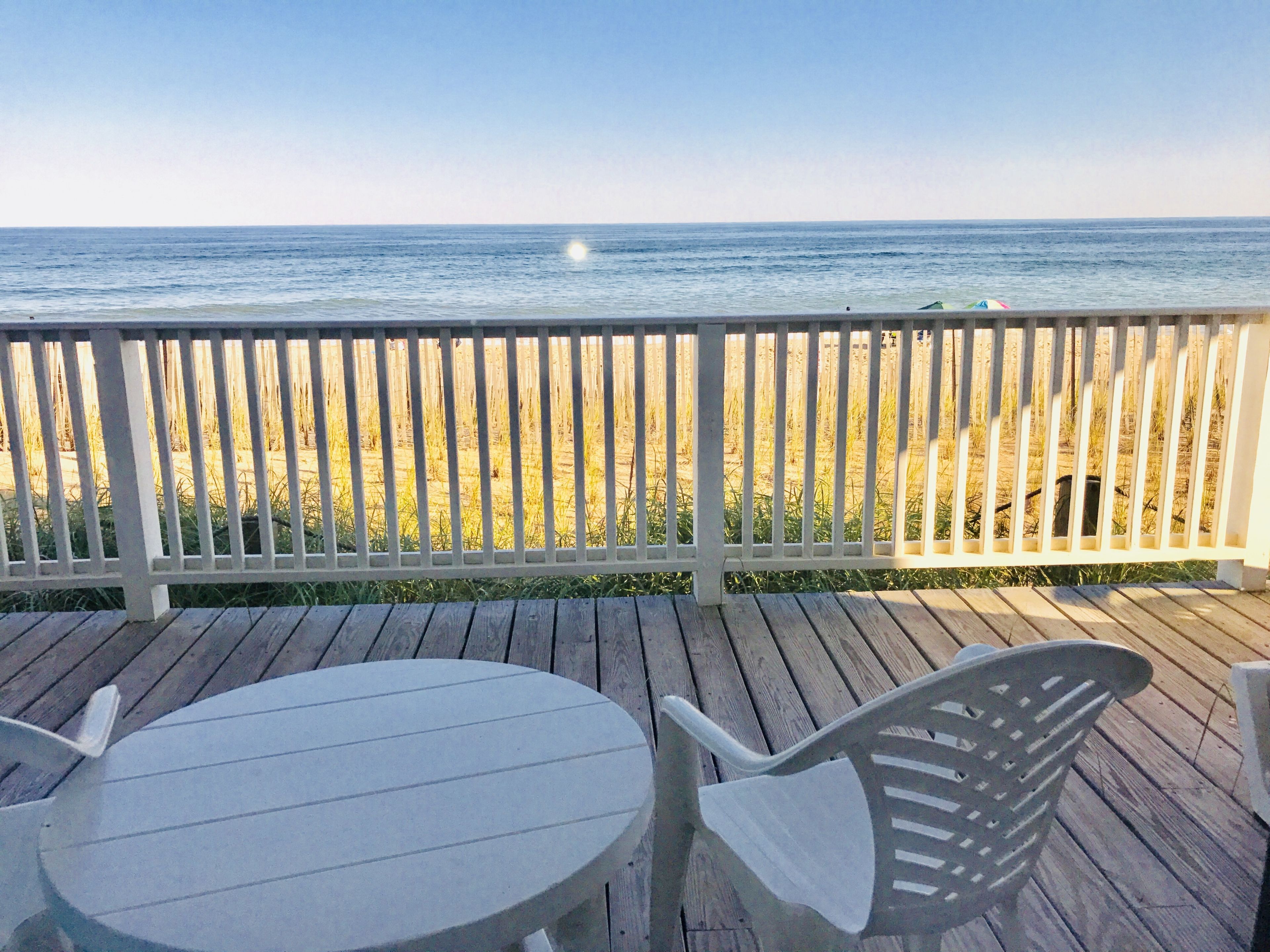 A wooden deck with a table and chairs overlooking a beach.