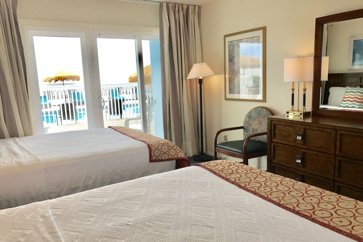 A hotel room with two beds, a chair, a dresser, a lamp, and a painting on the wall.