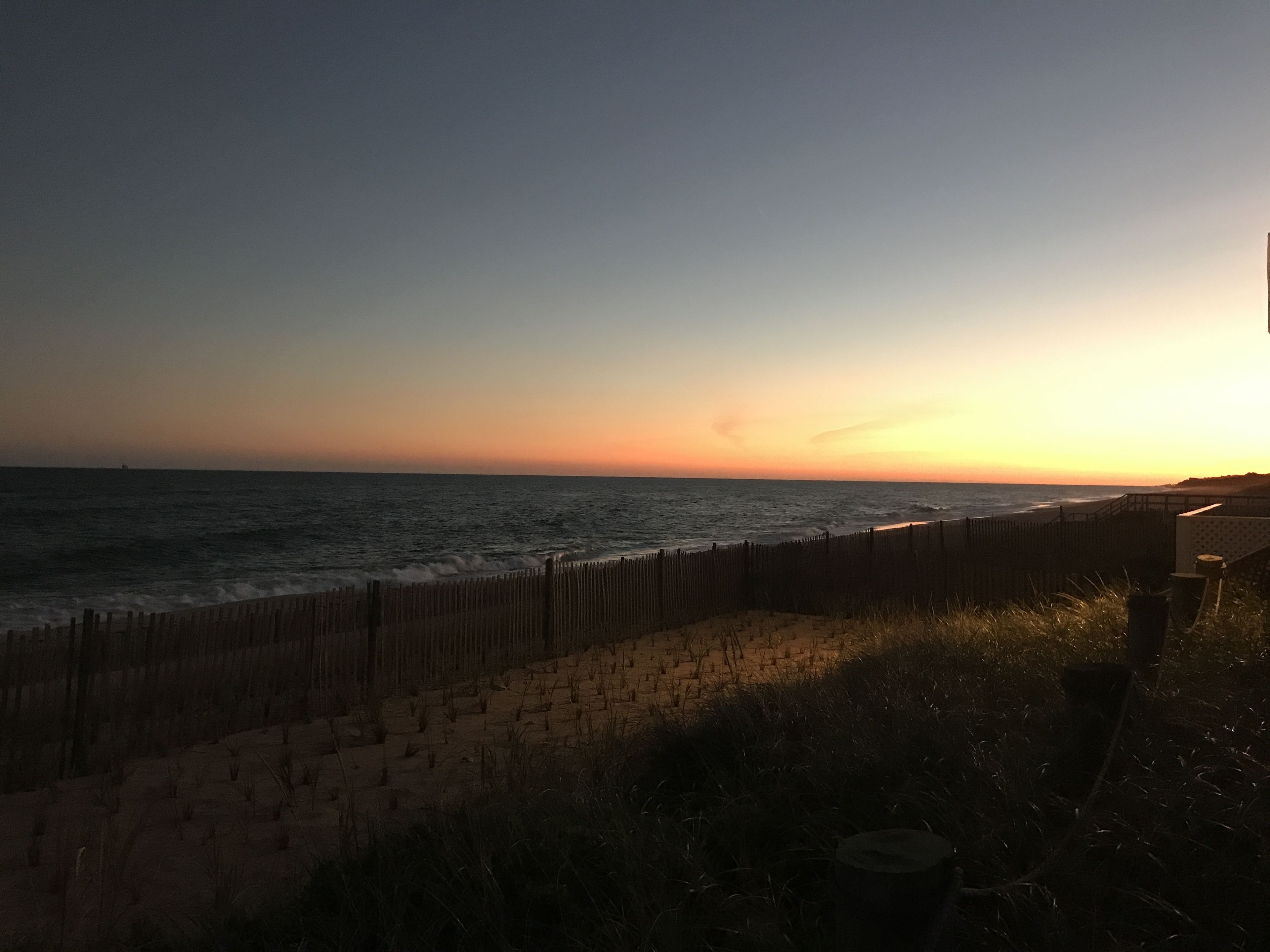 A beach with a wooden fence and a sandy path leading to the water.