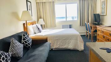 A hotel room with a bed, a desk, a chair, a TV, and a window with curtains.