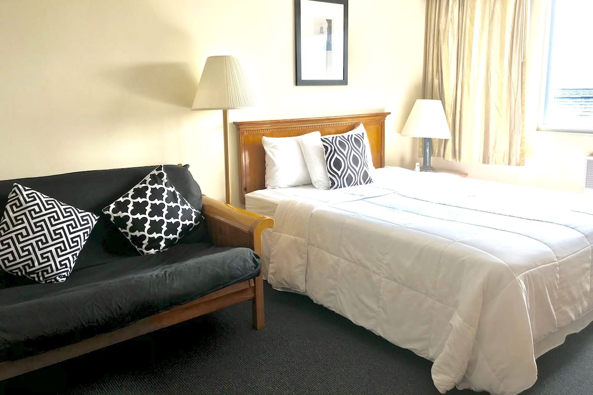 A hotel room with a bed, a sofa, two lamps, a framed picture on the wall, and a window with curtains.