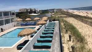 A pool area with lounge chairs and a pool, overlooking a beach with a wooden fence and beachgoers. - Ocean Surf Resort (Montauk)