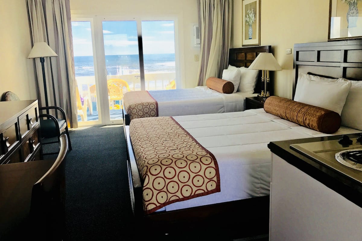 A hotel room with two beds, a desk, a chair, and a balcony with a view.