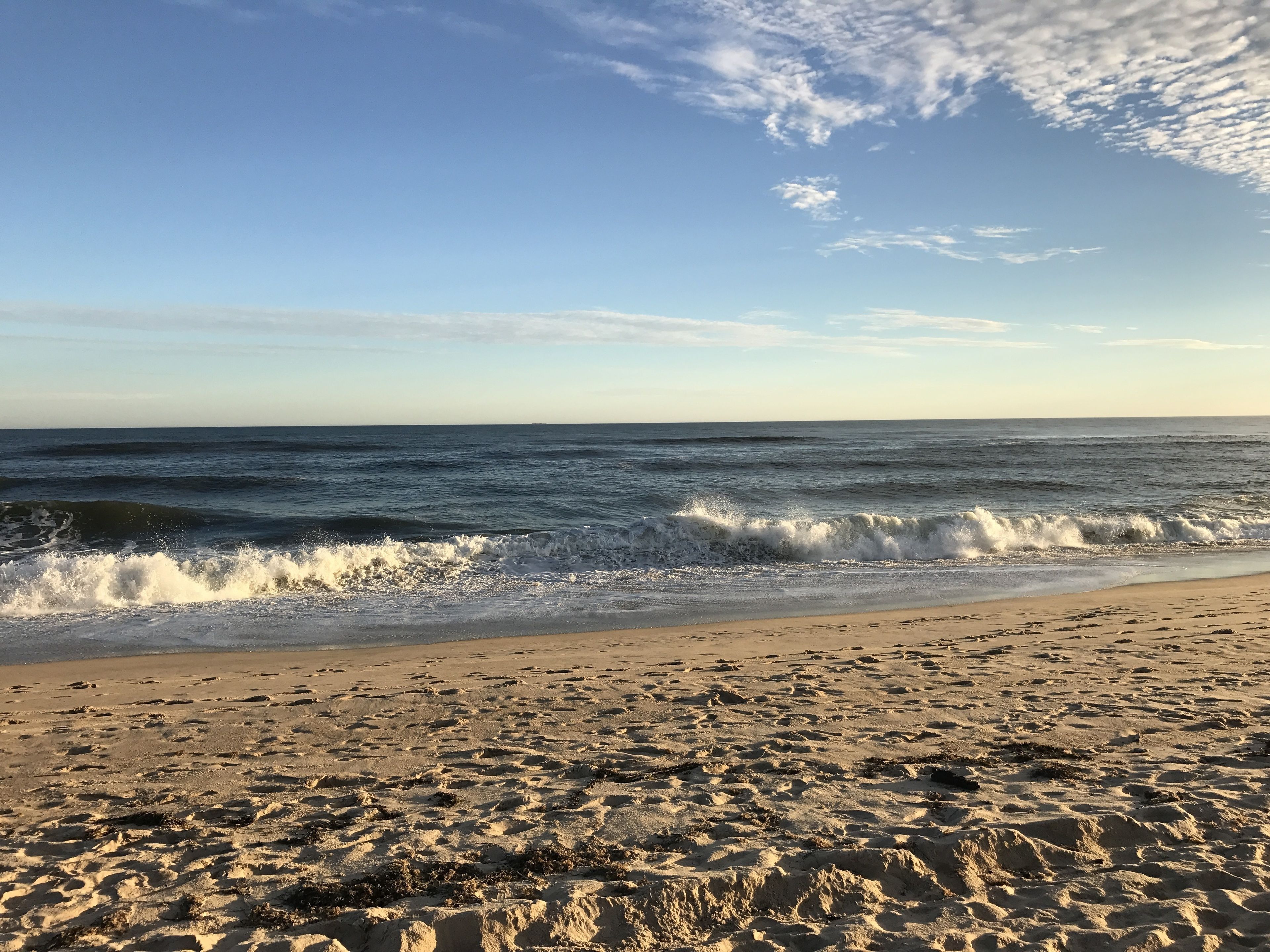 A beach with waves crashing onto the shore, clear skies, and a sandy beach.