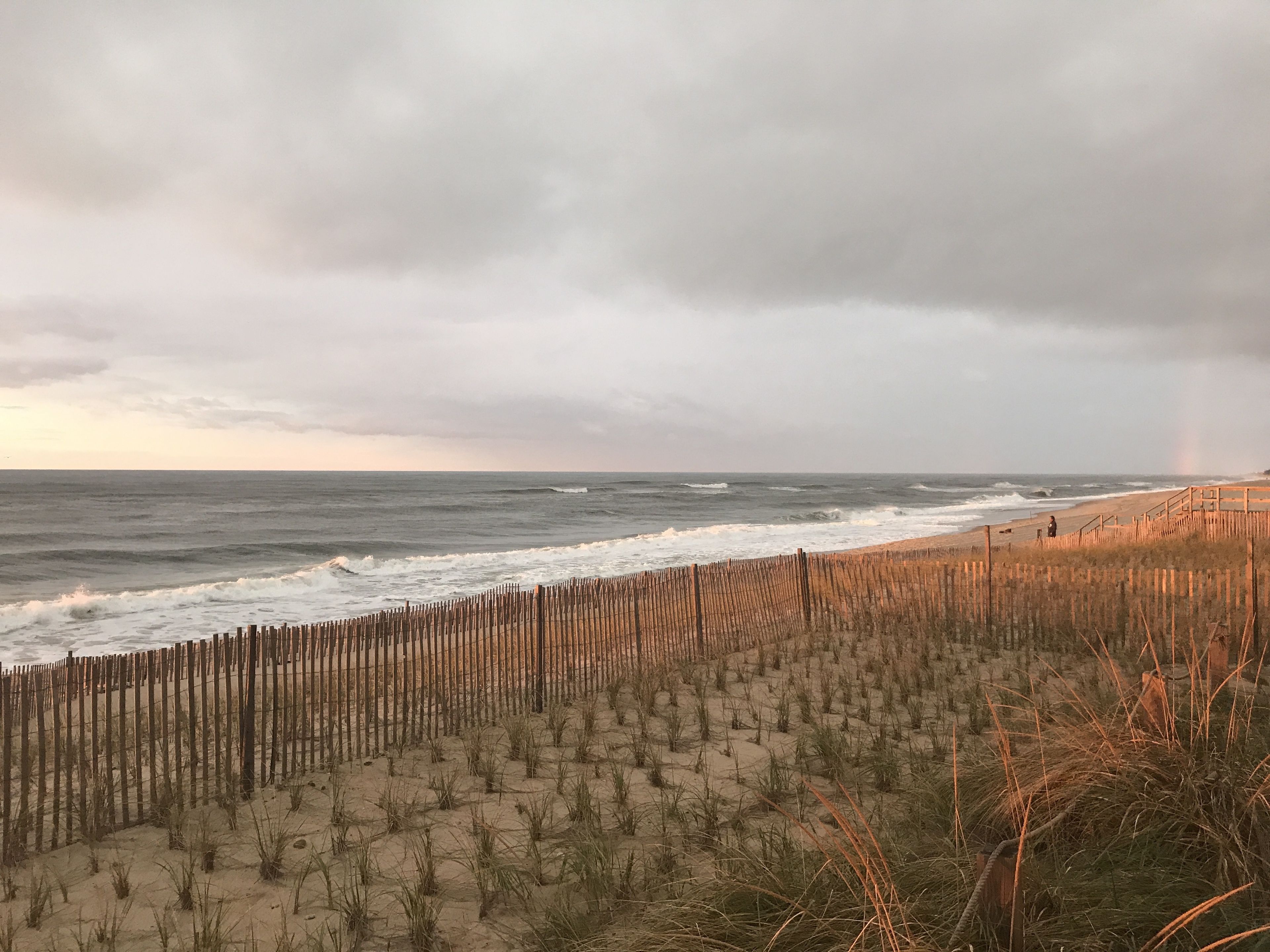 A beach with a wooden fence and waves crashing onto the shore.