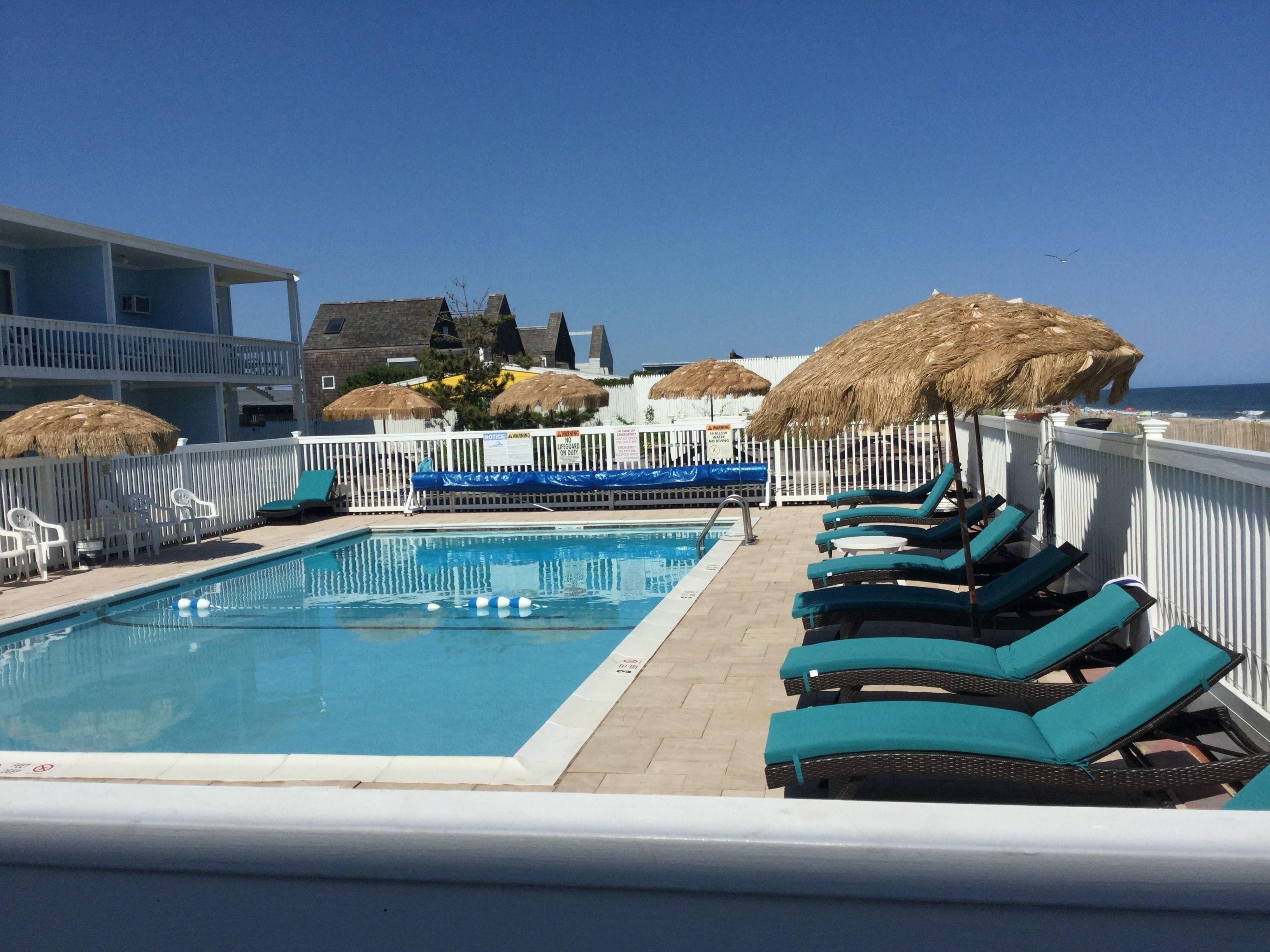 A pool area with lounge chairs and thatched umbrellas, overlooking a beach.