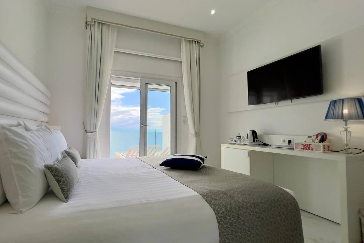 Habitación de hotel con cama, escritorio, televisión y vista al océano.