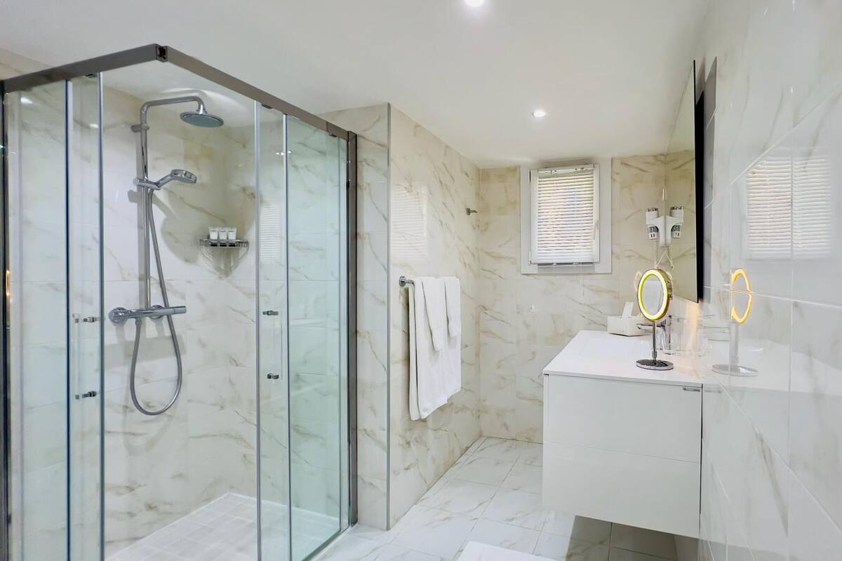 Un baño moderno con ducha de vidrio, tocador blanco con espejo y paredes de mármol.