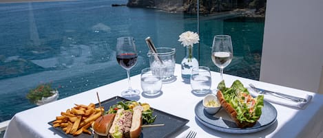 Une table dressée avec un repas, des verres et une vue sur la mer.