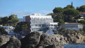 A coastal building with multiple balconies, surrounded by rocky terrain and trees. - Hôtel La Calanque (Cavalaire-sur-Mer)