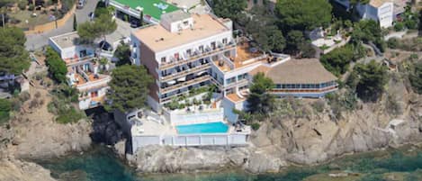 Une propriété située sur la côte, dotée d’une grande piscine, de plusieurs bâtiments et d’un rivage rocheux.