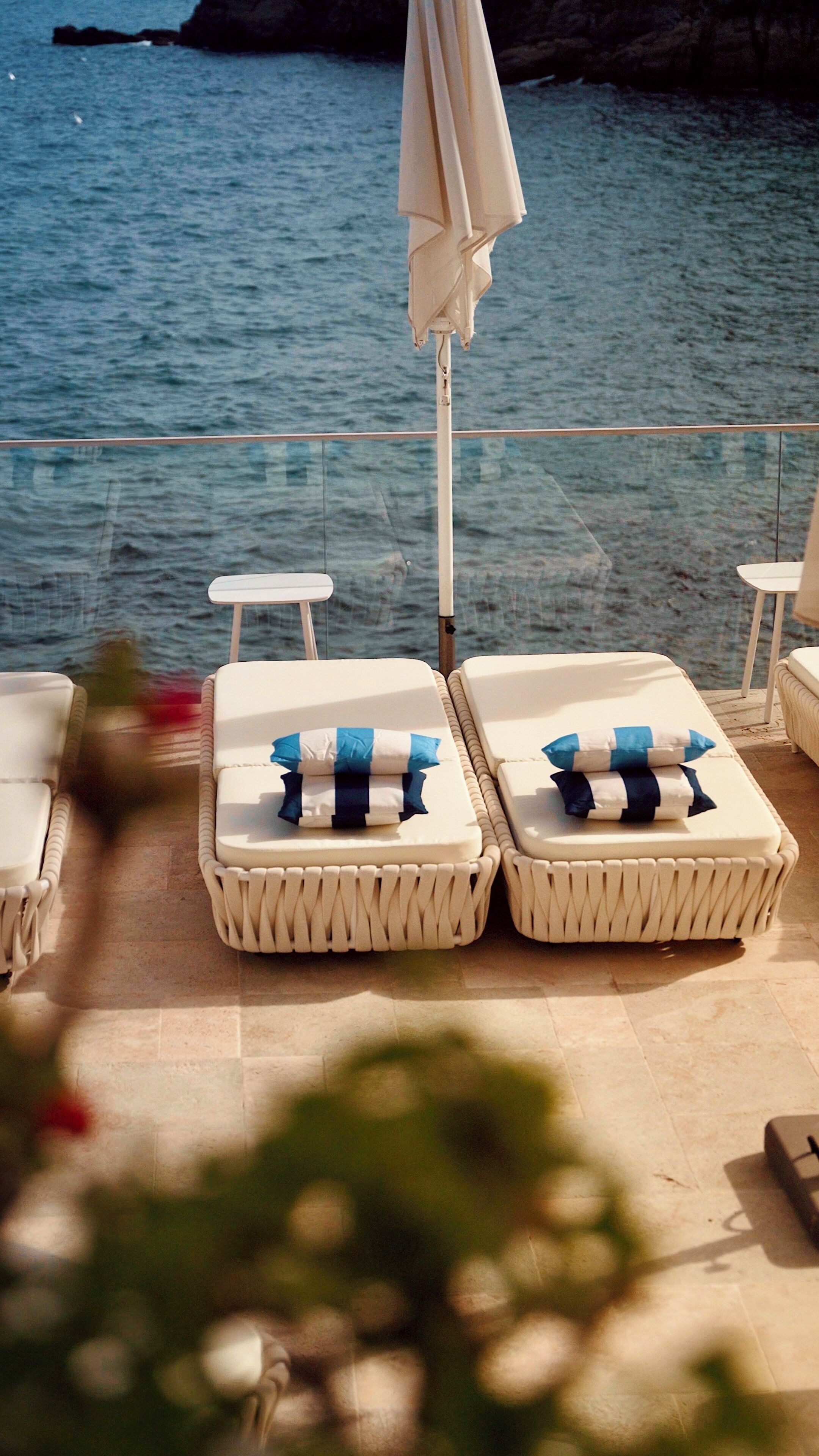 Une terrasse en bord de mer, avec des chaises longues et un parasol.