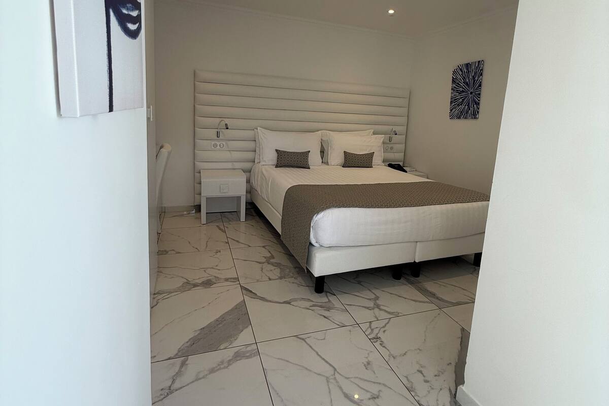 Un dormitorio moderno con una cama grande, una mesita de noche, una obra de arte en la pared y suelo de mármol.