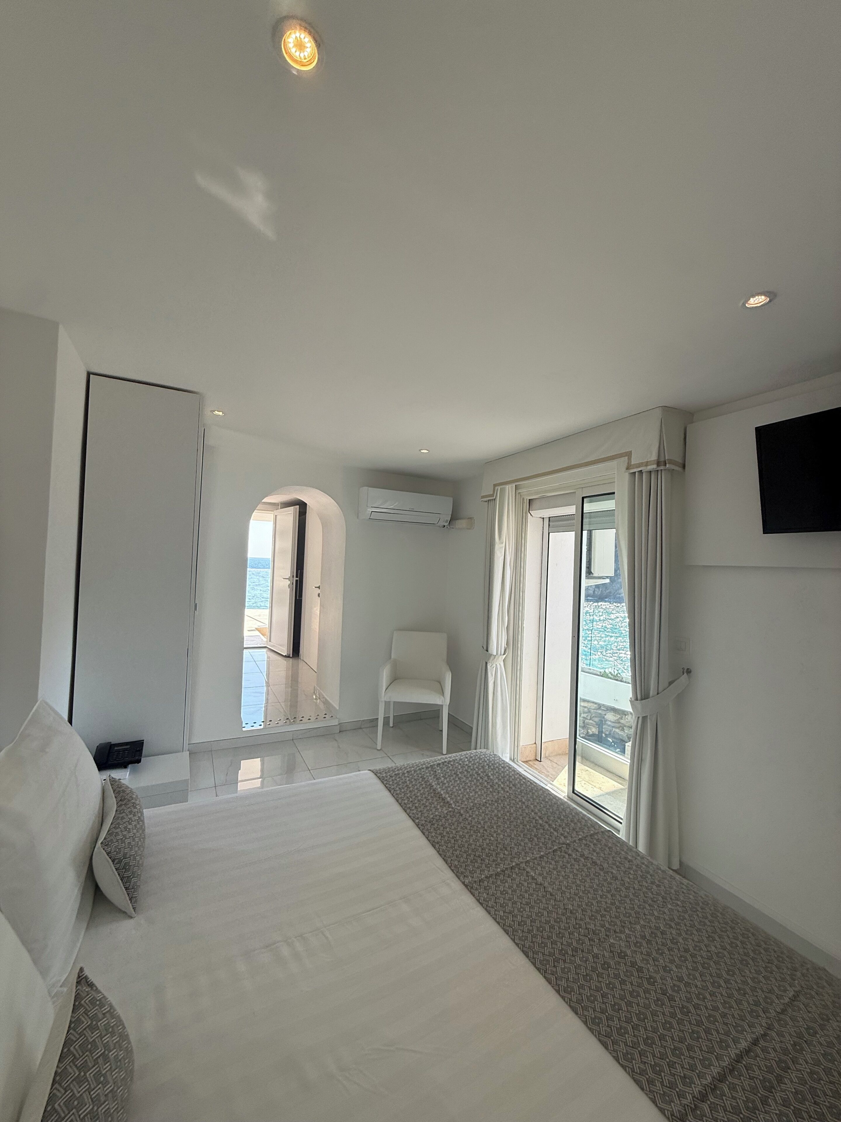 A hotel room with a bed, a chair, a TV, and a view of the outdoors.