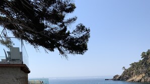 A seaside patio with white wicker furniture, a glass table, and a view of the sea. - Hôtel La Calanque (Cavalaire-sur-Mer)